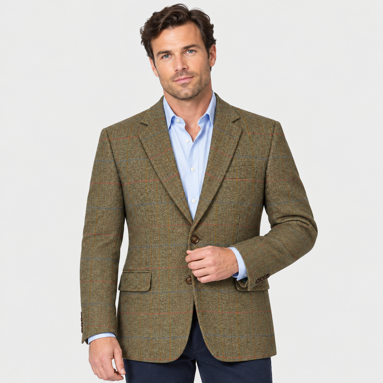 Male model wearing an olive-brown checked tweed jacket over a light blue shirt, with navy trousers against a white studio background.