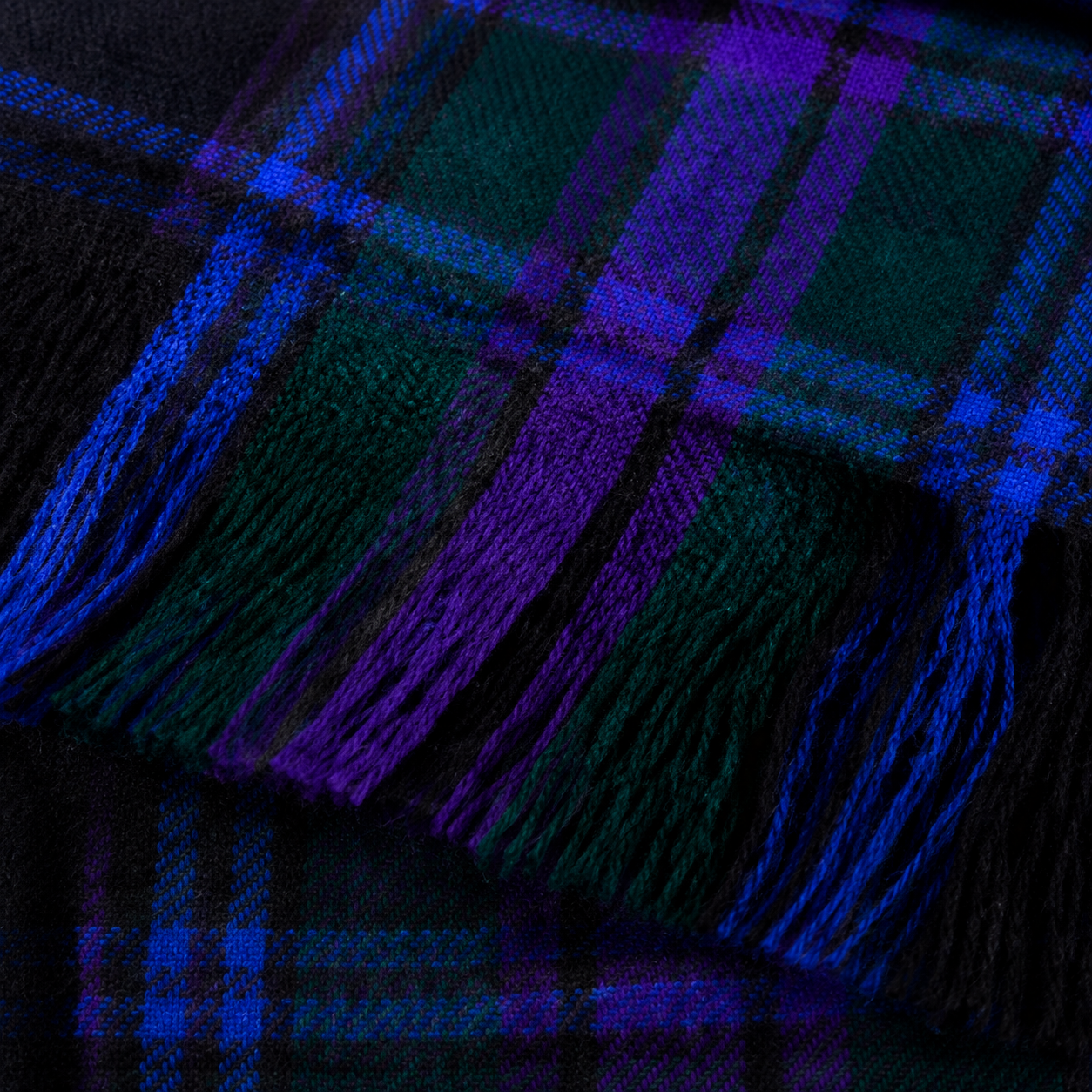 Detailed close-up of the heavyweight tartan fly plaid showing the woven purple, blue, green and black pattern and hand-finished fringe.
