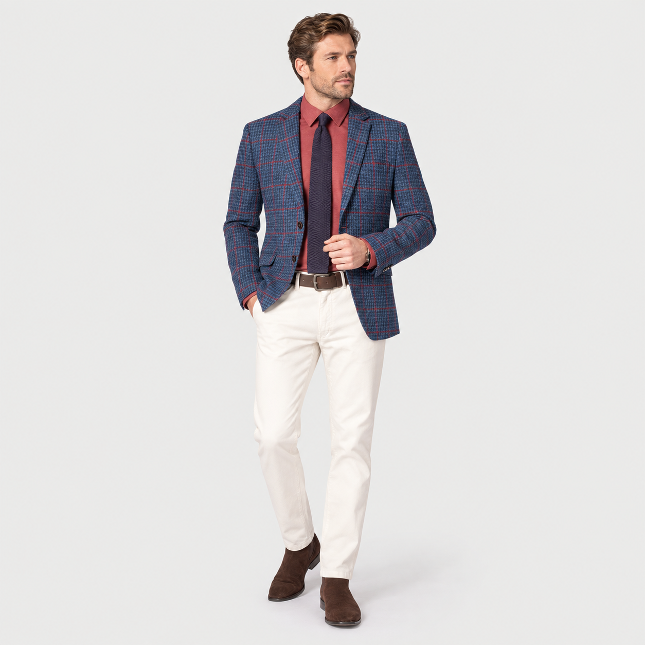 Front three-quarter view of a men’s blue checked tweed tailored fit jacket styled with a burgundy shirt, navy tie and light trousers.