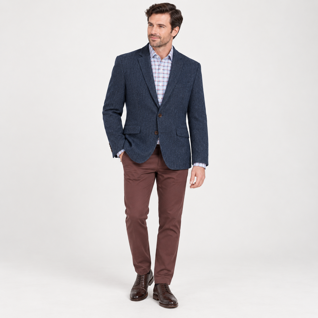 Full-length front view of a male model wearing a navy herringbone tweed jacket with a checked shirt and brown trousers.