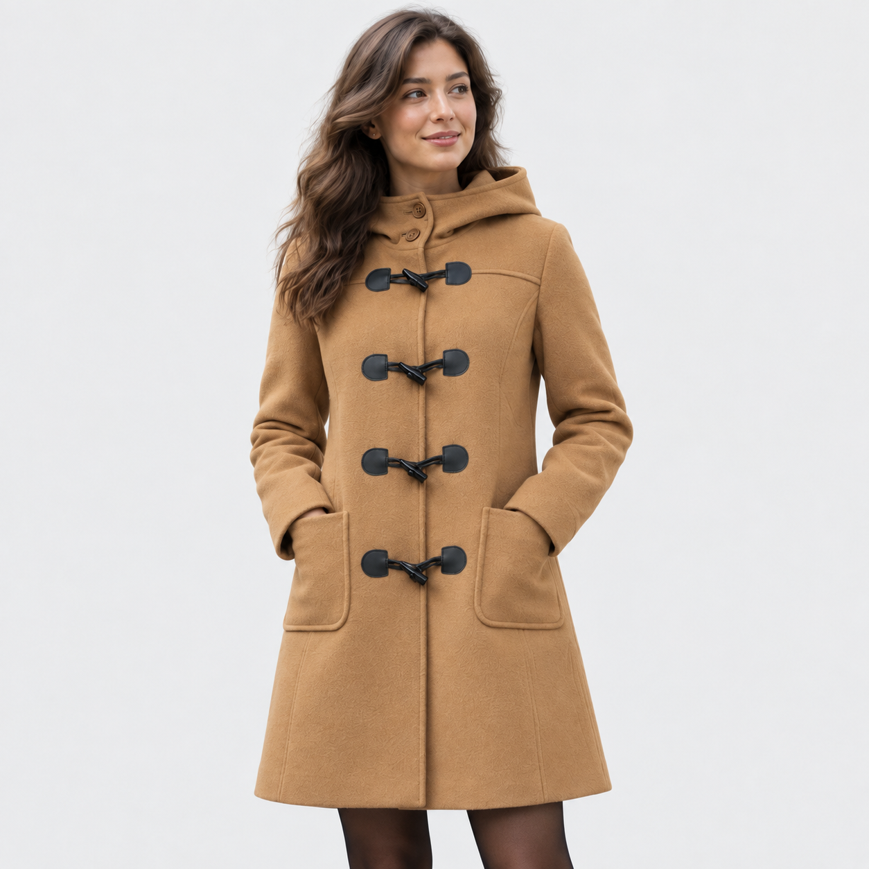 Woman modelling the camel duffle coat against a light studio background, with both hands in the front pockets.