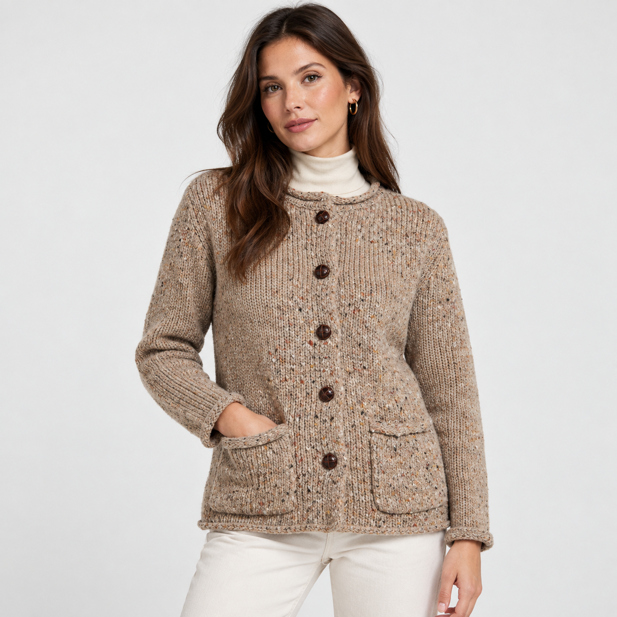 Woman wearing an oatmeal flecked knitted cardigan with dark buttons, two front patch pockets and a cream roll-neck top.