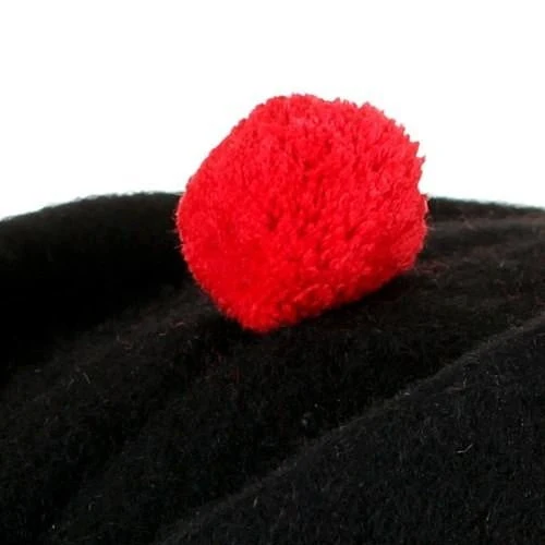 Close-up of the bright red wool toorie on top of a traditional black Scottish diced Glengarry Highland cap.